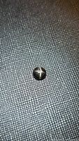 Single photo showing a small round black star diopside gemstone with a 4-ray star pattern on its polished cabochon surface, placed on textured dark fabric.