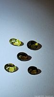 Five oval faceted multicolored tourmaline gemstones on white background with strong lighting showing color variation and facets