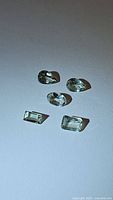 Five faceted natural tourmaline gemstones with off white and light green colors placed on white background under light.