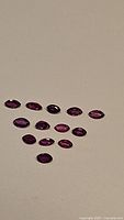 Fourteen natural untreated marquis cut rubies arranged in rows, showing varying deep red to purplish hues and good clarity.