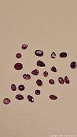 Natural untreated rubies of various shapes and cuts laid out on a neutral background showing color and size variety.