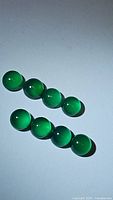 Eight natural vivid green onyx round cabochon beads arranged in two rows on a light background, showing smooth polish and bright green color