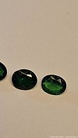Photo of three oval-cut vivid green Tsavorite garnet gemstones laid flat to show color and cut