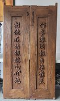 Front view of two large solid wood doors with hand-carved Chinese characters vertically inscribed on inset panels.