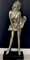 Full front view of silver-tone Marilyn Monroe statue standing on black base, showing iconic skirt-blowing pose and detailed facial expression.
