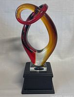 Front view of MCM hand blown art glass sculpture on black pedestal base with amber, red, black coloring and loops.