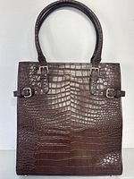 Front view of the brown croc embossed Kate Spade handbag with two shoulder handles and buckle accents.
