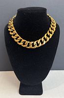 Front view of a chunky gold-tone chain necklace displayed on a black bust.