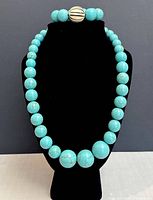 Frontal view of turquoise bead necklace and matching bracelet on black display stand showing bead size and color.