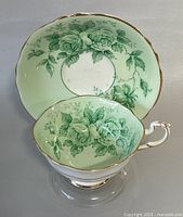 Top-down view of teacup inside matching saucer showing green floral designs and gold accents.