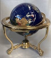 Front view of 16-inch globe with deep blue oceans and precious stone continents on a solid brass stand.
