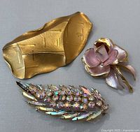 Three vintage brooches including two pink and gold floral brooches and one gold-tone rhinestone leaf brooch laid flat