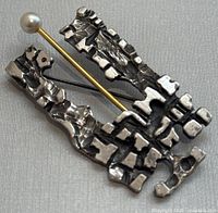 Front angled view of the abstract textured pewter brooch with attached pin and pearl accent, showing the intricate Brutalist design and its metal textures.