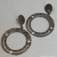Front view of two textured pewter circular earrings with hammered finish and cutouts, laid flat.