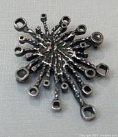 Front view of vintage pewter brooch shaped like a fireworks burst with textured rods ending in hollow squares and circles.