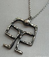 Close-up view of the abstract brutalist pewter pendant on the 20-inch chain, showing textured finish and pendant detail.