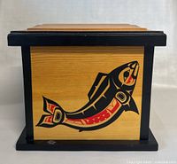 Front side of wooden art box showing stylized fish design in black and red on wood with black frame edges.
