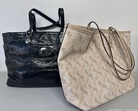 Two Coach tote bags side by side showing front and side angles; one black patent leather with embossed 'C' pattern and silver charm, other beige canvas with horse and carriage print.