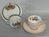 Two vintage Aynsley teacups with matching saucers shown upright, highlighting the crown and floral designs, gold rims and detailing.