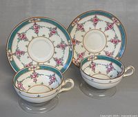Two vintage English Minton teacups with matching saucers shown together, highlighting the floral and turquoise band decoration with gold trim.