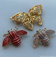 Front view of the three brooches: gold-tone filigree butterfly with faux pearl, red and lavender enamel bee brooches with rhinestone eyes.