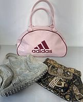 Front view of all three bags showing Adidas pink patent leather bag, gray Alexander Wang handbag, and Guess patterned crossbody bag with buckle