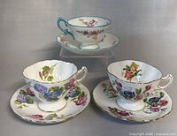 Front view of all three vintage English Hammersley teacups with matching saucers showing floral designs and gold trim.
