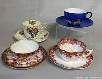 Four vintage teacups with matching saucers displayed on a neutral background showing diverse styles and floral designs
