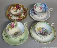 Four vintage English teacups with matching saucers, each featuring distinct floral patterns and gold trim, arranged in a 2x2 layout on a flat surface.