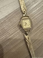 Close-up of the gold-toned rectangular watch face showing the off-white dial with index markers, black hour and minute hands, and 'Caravelle' branding.