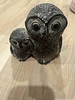Photo showing full soapstone carving of mother owl with baby on wooden floor, highlighting size and shape.