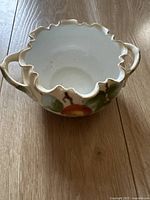 Top and side view of antique porcelain bowl showing ruffled edge, dual handles, and painted fruit and flower design with gold accents.