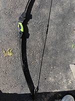 Full view of black recurve archery bow with curved limbs lying on asphalt ground, showing overall length and design