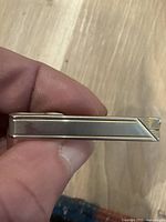 Close-up side view of gold-tone metal tie clip showing clasp and brushed metal design.