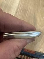 Side view of gold metal tie clip showing smooth body and slight curvature
