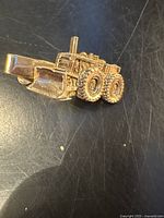 Front view of gold-tone metal tie clip shaped like a bulldozer or heavy machinery vehicle, showing detailed sculpting and tires.