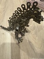 Angled front-left view of dinosaur sculpture showing detailed head, body, and distinctive back plates made from washers and metal pieces.