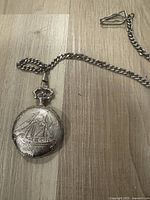 Photo showing the full length of the silver toned chain attached to the pocket watch with embossed sailing ship design.