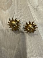 Front view of two gold sunburst metal cuff links with face motif.