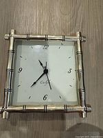 Front view of the silver plated Carlyle alarm clock with white clock face, black numbers and hands framed in a bamboo-style silver frame.