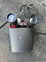 Top view of binoculars partially out of black leather case showing large front lenses and leather straps