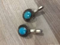 Blurry photo showing two round silver-tone cufflinks each with a central smooth turquoise stone and detailed decorative border with clip back mechanisms.