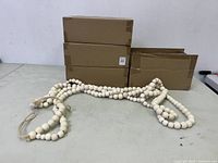 Four cardboard boxes stacked in the background, with several wooden bead garlands displayed in front showing size and detail.