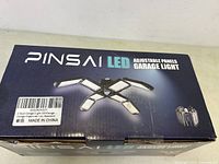 Box front showing brand PINSAl LED Adjustable Panels Garage Light with image of the adjustable panel light and packaging label indication new in box and made in China.