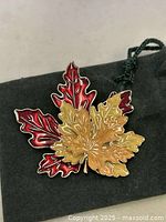 Front view of the autumn leaf enamel brooch resting on top of the black fabric dust case.