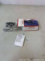 Bernina No. 86 Ruffles Foot metal sewing machine attachment, new in box with instruction manual laid beside it on table.