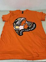 Orange T-shirt with 'Every Child Matters' graphic design on chest.