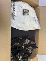 View inside the box showing a white padded jacket in packaging and a black floral print garment.