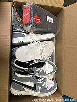 Box containing two pairs of shoes, one white slip-on and one black and white high-top sneaker, and boxed household items