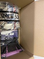 Box containing a folded plaid patterned clothing item in plastic packaging, partially visible brand name 'Andrew Sco'.